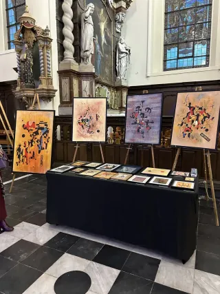 Colourful paintings and smaller artworks displayed among the historic furnishings of Sint-Denijskerk in Kalken